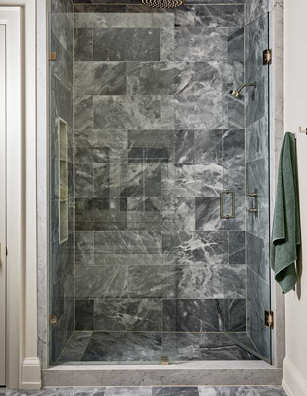 The shower in the principal bathroom is a grey blue marbled tile with a large glass door and a rain shower head. serene city retreat