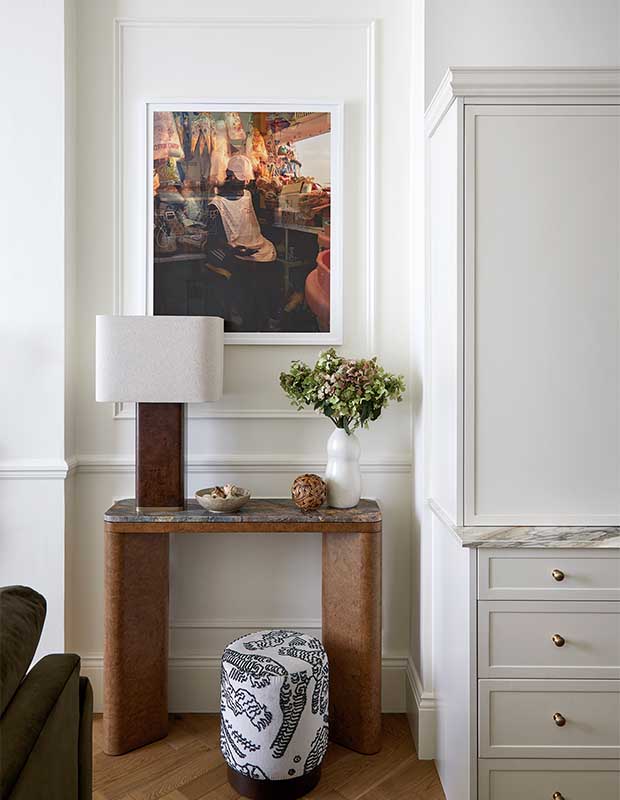 An alternate angle of the living room, which is painted white. there is a rounded table, rounded lamp, abstract art, and doodle-patterned stool. notting hill flat