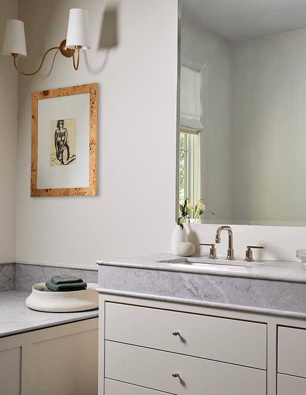 The principal bathroom has marbled countertops, brass elements, and a sink below a large mirror. serene city retreat