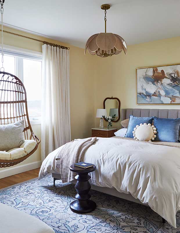 a pretty bedroom with a plush bed, hanging chair, pale yellow walls and a blue patterned carpet. Morrisburg budget reno. stylish budget reno