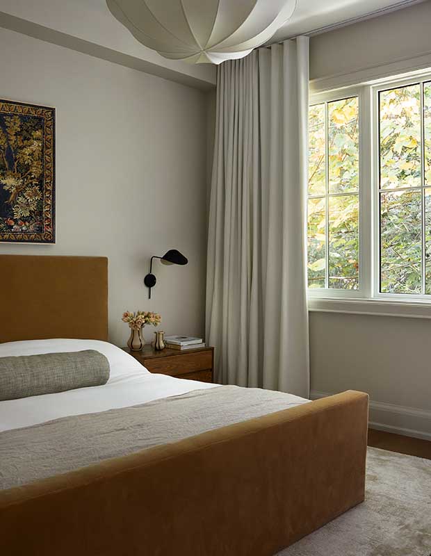 The principal bedroom has minimal grey elements, an artistic pendant light, nature themed art on the wall. The window is open and large, with many large plants and trees. serene city retreat