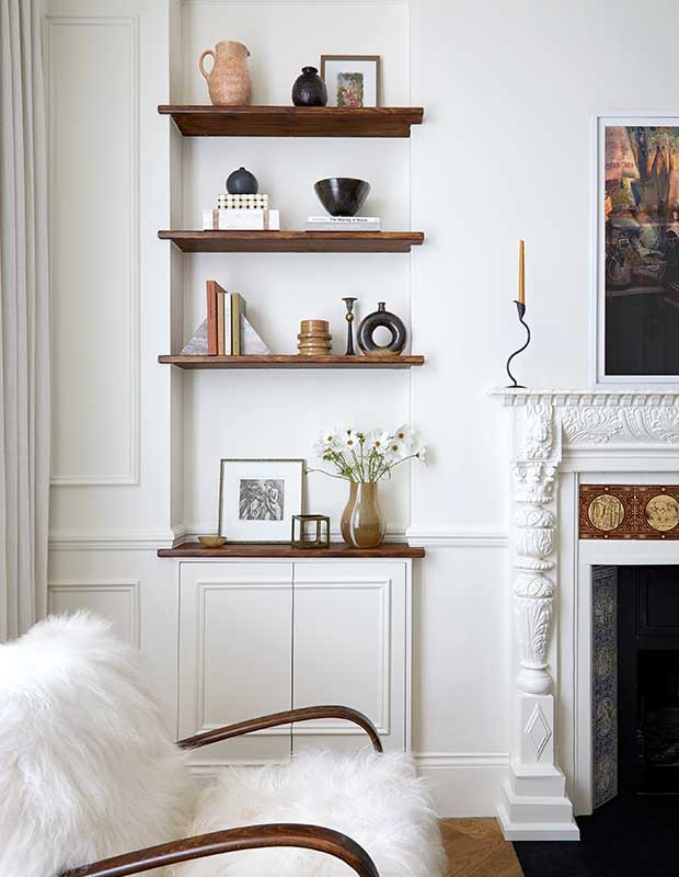 A white walled living room with moulding on the walls and walnut shelves that display various minimal trinkets. notting hill flat