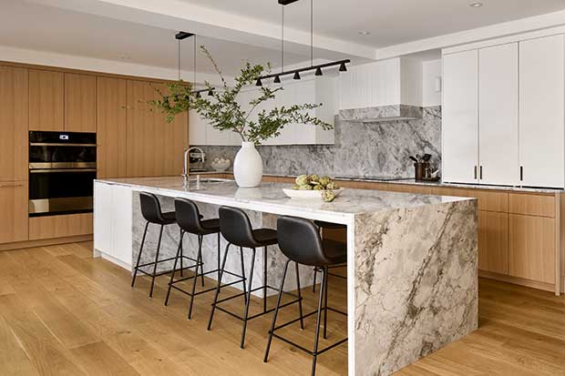 A large marble island is the centre of this light-oak kitchen with white uppers, oak cabinets and floors, and matte black accents. english cottage-style house