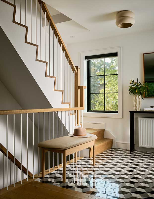 A modern entryway with a geometric tile floor, medium wood staircase leading both upstairs and down, and a matching bench. english cottage-style house