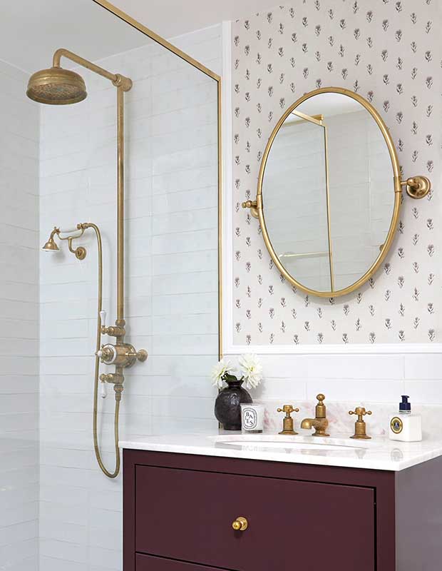 A retro inspired bathroom with floral printed wallpaper, brass accents on the shower and mirror, and white subway tiles. notting hill flat