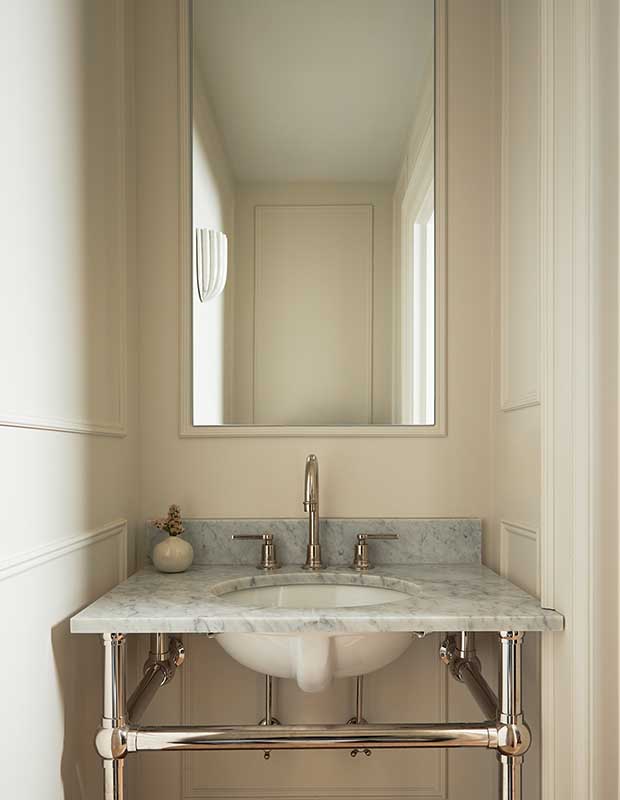 A white bathroom with marble countertops and silver fixtures. a large rectangular mirror reflects more white walls and modern artistic wall sconces. serene city retreat