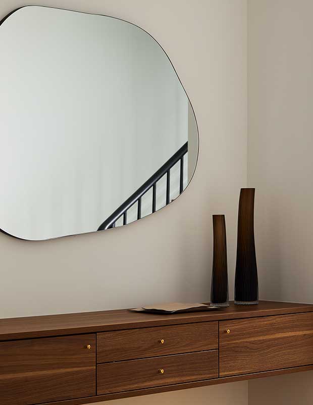 A walnut console sits below a large blob-shaped mirror. serene city retreat