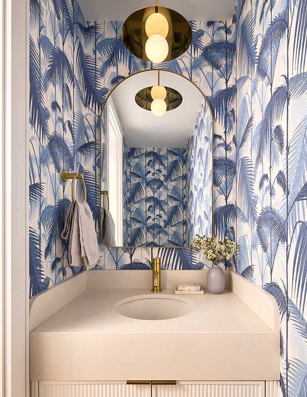 A blue jungle-inspired wallpaper lines the walls of this powder room with a cream vanity and gold accents. english cottage-style house