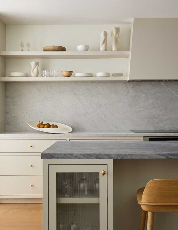 A cool-toned kitchen with marble backsplash and countertops, reeded glass cabinets under the island, and shelves lined with minimal glass and dinerwear. serene city retreat