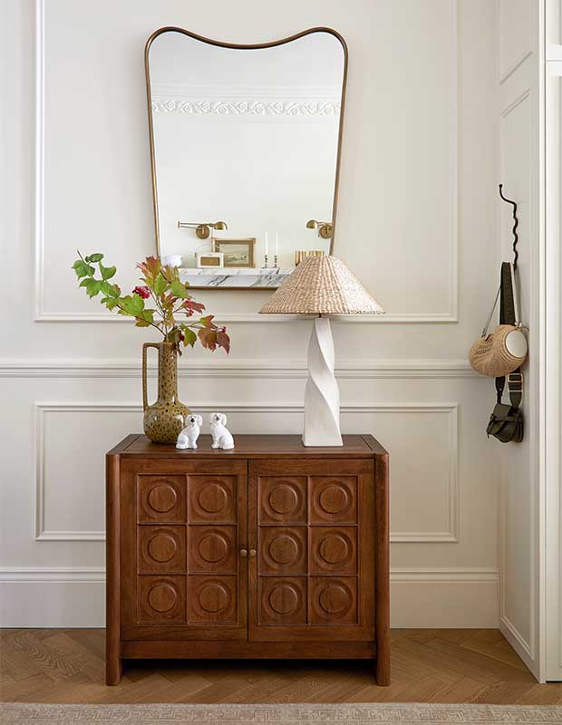 A portrait of a hallway nook with an MCM vintage console, a uniquely shaped brass mirror, two dog statuettes, and two funky vases. notting hill flat