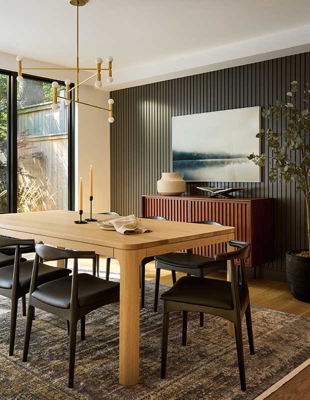 A sleek modern dining room with vertical reeded walls, a rounded light wood, dining table, modern black chairs and lighting fixtures. english cottage-style house