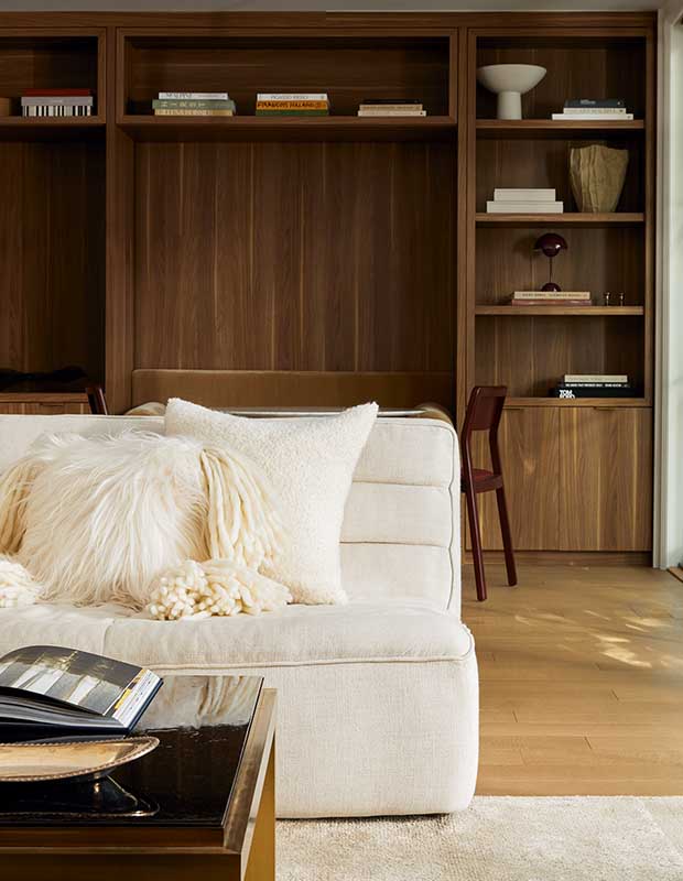 A plush white couch with fuzzy pillows sits in front of a large walnut bookcase and banquet area. serene city retreat