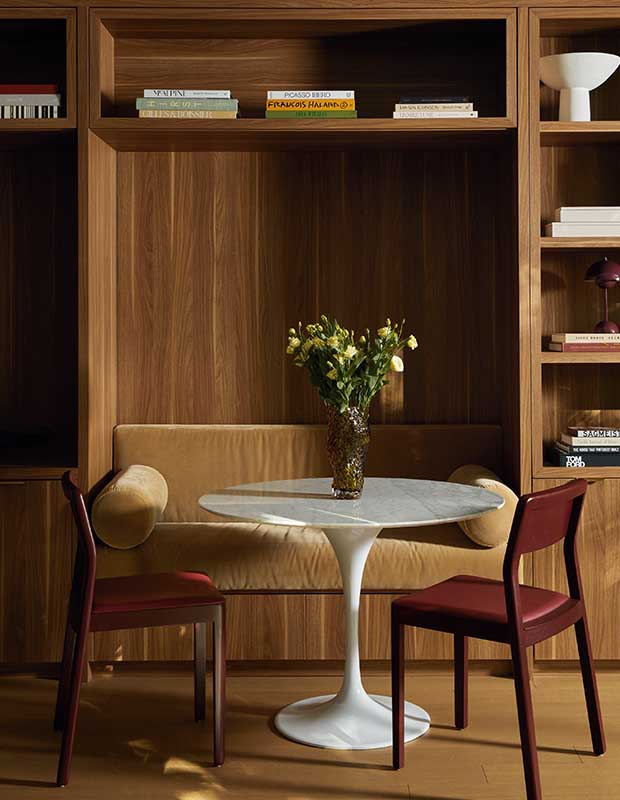 A warm walnut wood banquet area with a plush cushion and tall shelves with books placed neatly on them. serene city retreat