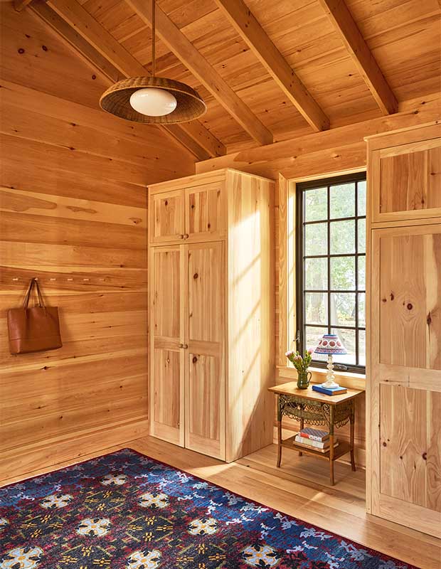 A pine-walled entryway with two large closets, pegged hooks, and a red and blue patterned rug. wood-clad family cottage