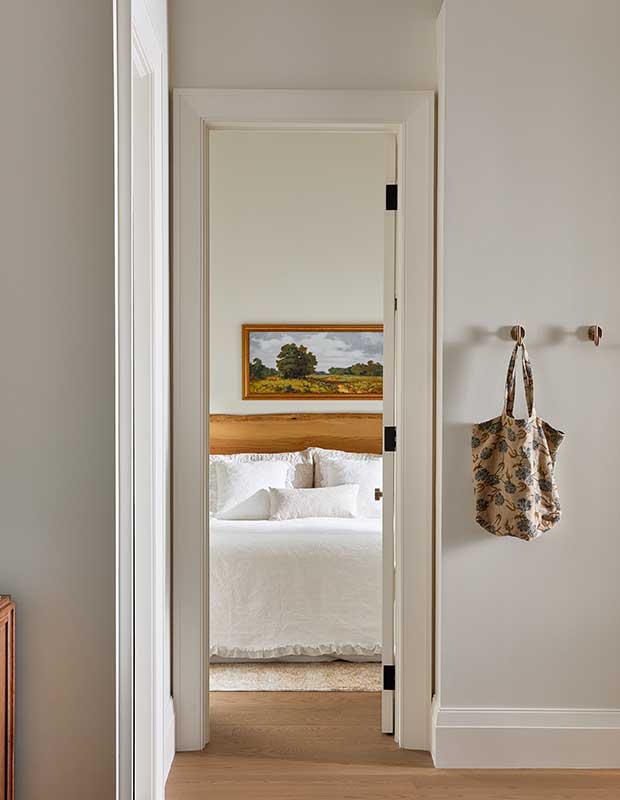 An outside view of a principal bedroom, which has a wood headboard and a nature painting. Outside the bedroom, a tote bag hangs on hooks. serene muskoka bunkie