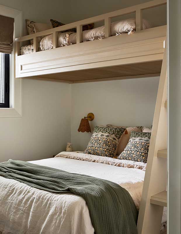 A bedroom with one larger bed, and a blonde wood bunk bed overtop. The cream bedspreads are accented with sage green and burnt orange. serene muskoka bunkie
