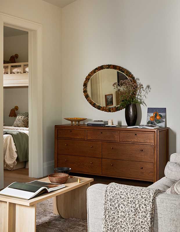 An off-white walled living room with a dark wood dresser that sits below an ovular mirror. serene muskoka bunkie
