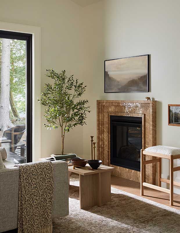 An off white-walled living room with a stone fireplace, grey and pale brown furniture, and organic elements. serene muskoka bunkie