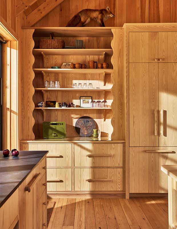 A pine shelving unit with rustic decor and glasses. A taxidermy fox sits on top of the unit. The unit itself has wavy side pannels and a second portion with doors. wood-clad family cottage