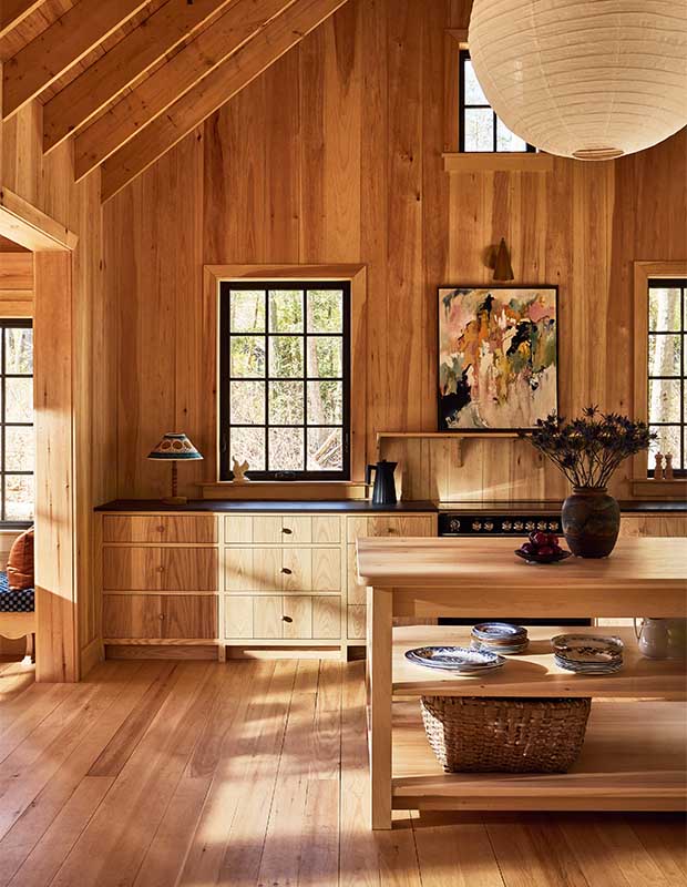 A pine kitchen with slanted ceilings and open wood beams. The furniture matches the walls, and a large circular lantern light.wood-clad family cottage