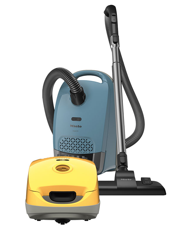 This photograph features two small vacuums (eco-friendly items) on a white background. The vacuum in the foreground is bright yellow, and the vacuum in the background is a moody blue.