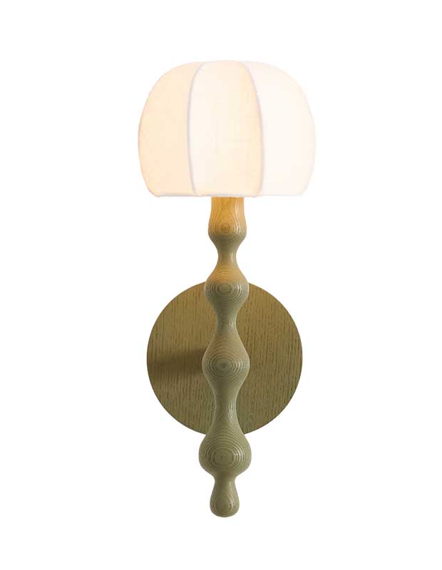 A photo of a statement sconce made of wood and stained a neutral green. The sconce has a narrow post with whimsical bulges and is topped with a linen shade in a segmented dome shape.