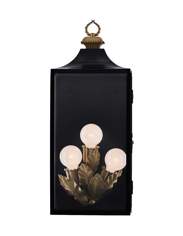 A photo of a statement sconce in a black, square lantern shape with three bulbs in the interior with brass leaf motifs.