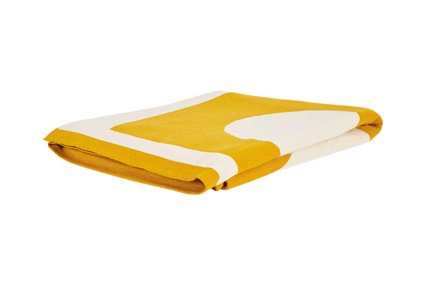 A bright yellow and white abstract-patterned throw lies folded against a white background.