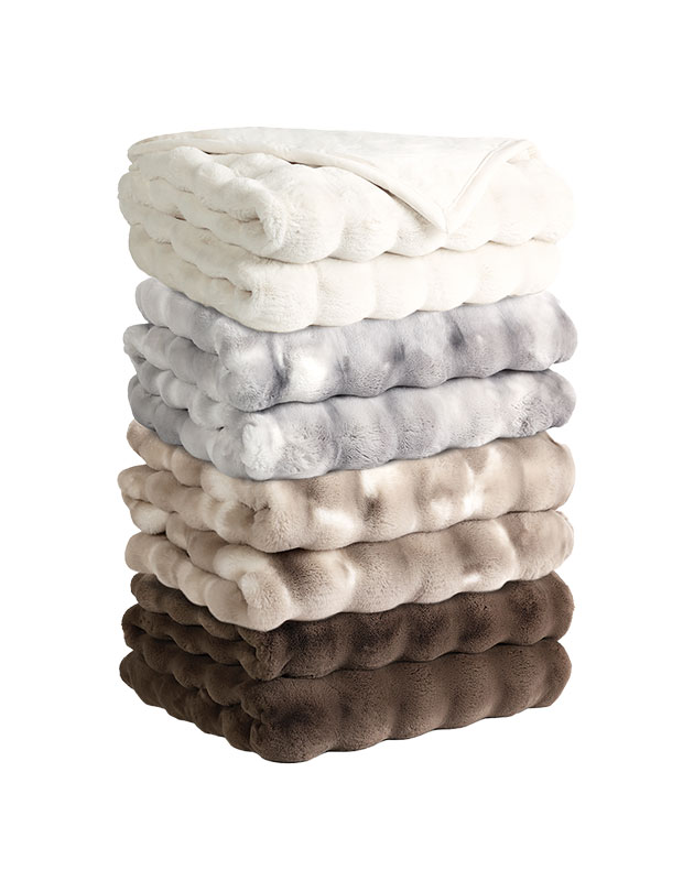 A stack of faux fur stylish throws folded in a pile against a white background. There are four of them: one brown, one beige, one grey and one white.