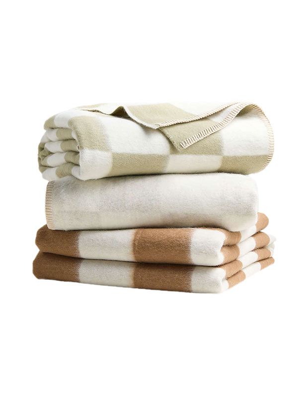 Three folded stylish throws with checkered patterns are stacked on a white background.