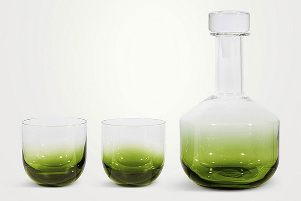 Photograph of a sustainable gift: A glass decanter sits to the right of two whiskey glasses. All of them are made of dark green glass at the bottom fading to clear glass at the top.