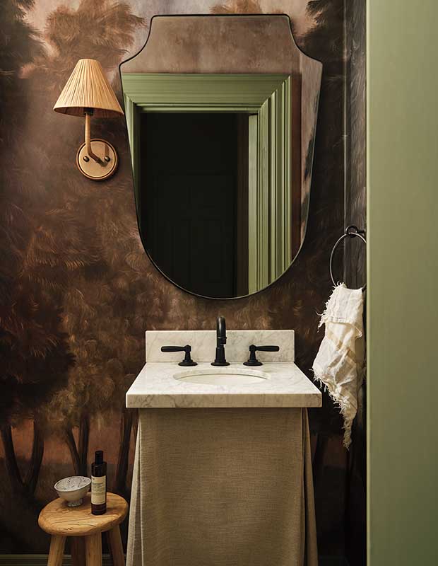 A photograph of a powder room with brown walls, a white sink, and a decorative mirror reflecting a green doorframe.