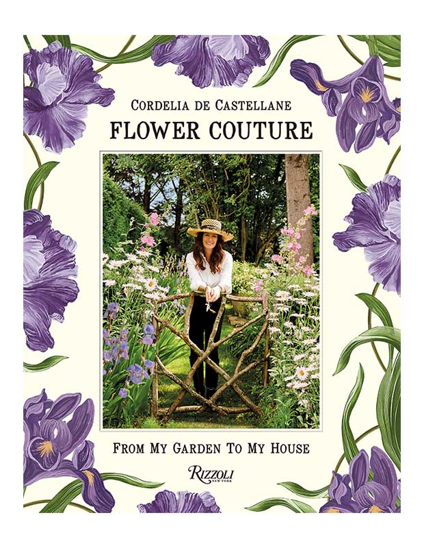 The cover of design book "Flower Couture." In the centre is a photo of a white woman in a white shirt and black pants wearing a straw hat leaning on a garden fence surrounded by flowers. Around the photo is a wide cream border adorned with purple flowers with green leaves.