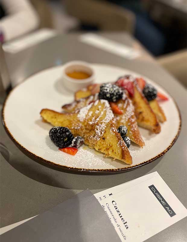 A picture of breakfast at the AC Old Montreal hotel. A white plate on a grey table has four slices of french toast topped with blackberries and strawberries.