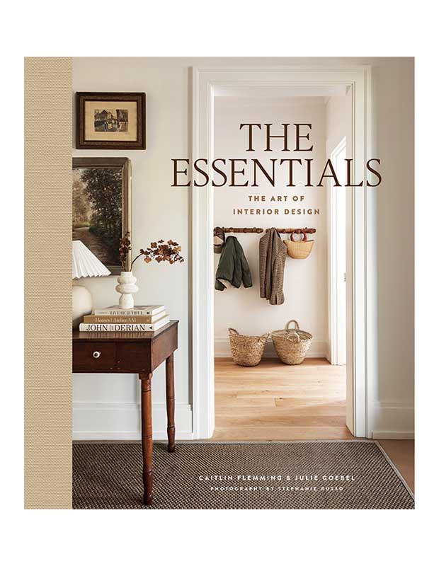 The cover of the design book "The Essentials." The title is superimposed in brown letters over a photograph that looks through a doorway in a room to a hallway with some clothes on a hanger.