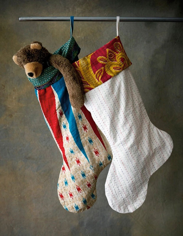 Photograph of sustainable gift: Two handmade stockings hanging against a brown background, one with a stuffed teddy bear hanging out of it.
