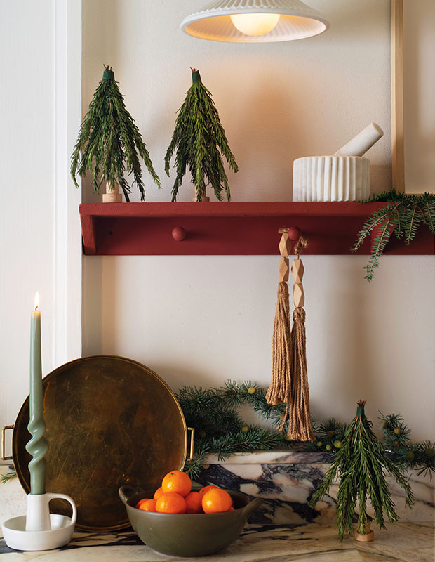 A photograph of a holiday craft: two small trees on a red shelf above a green candle.
