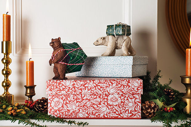 A photograph of a holiday craft: two toy bears with presents tied to their back sit on wrapped boxes on a shelf.
