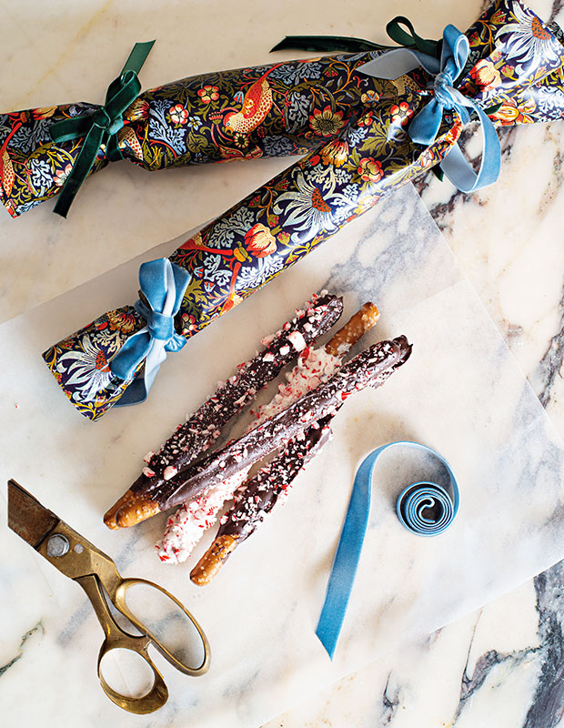 A photograph of a holiday craft: Two patterned Christmas crackers and a package of preztel sticks dipped in chocolate with sprinklings of candy cane.