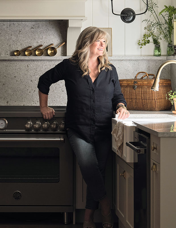 Kitchen with farmhouse aesthetic: A photograph of a woman with blonde hair and a black shirt leaning against a kitchen sink.