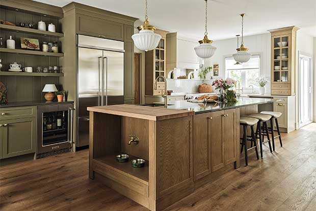 Kitchen with farmhouse aesthetic: A shot of a kitchen island with three white pendants hanging above it. On the end of the island, a faucet above two dog bowls is visible.