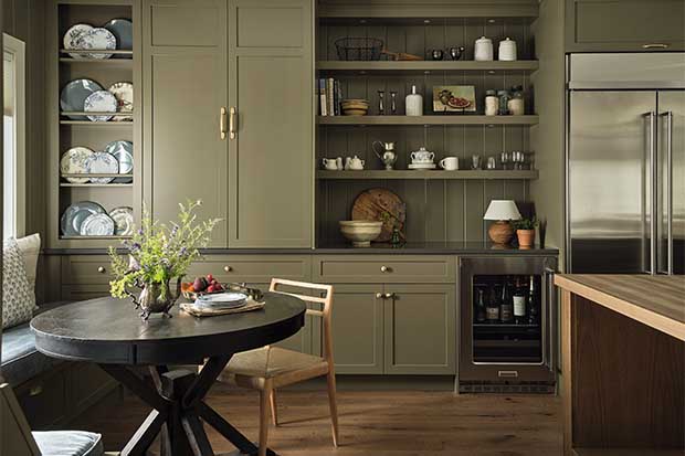 Kitchen with farmhouse aesthetic: Open shelves filled with vintage pots and doodads and a green cabinet sit behind a dark, round table.