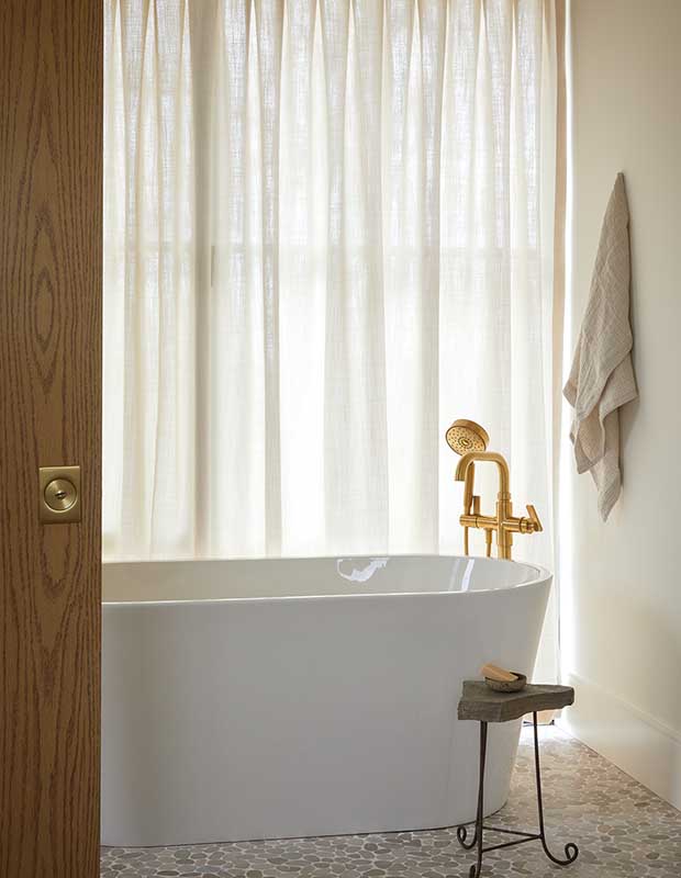 Photo of house featuring English design: A freestanding bathtub with a shiny brass faucet and a towel hanging on the wall.