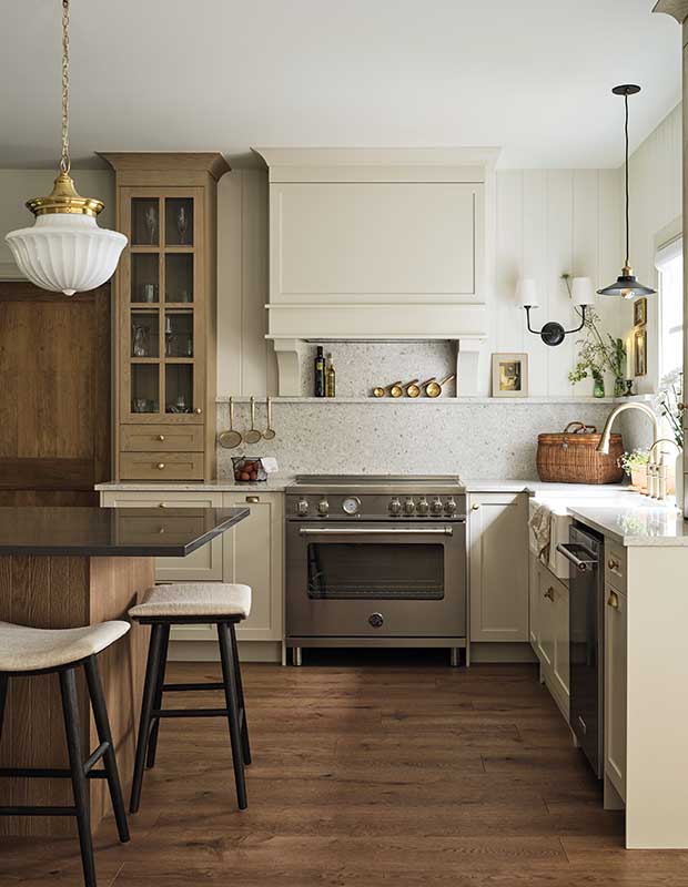 Kitchen with farmhouse aesthetic: A photograph of a kitchen range with a white vent hood above it. On the left is a kitchen island, and on the right is a kitchen sink.