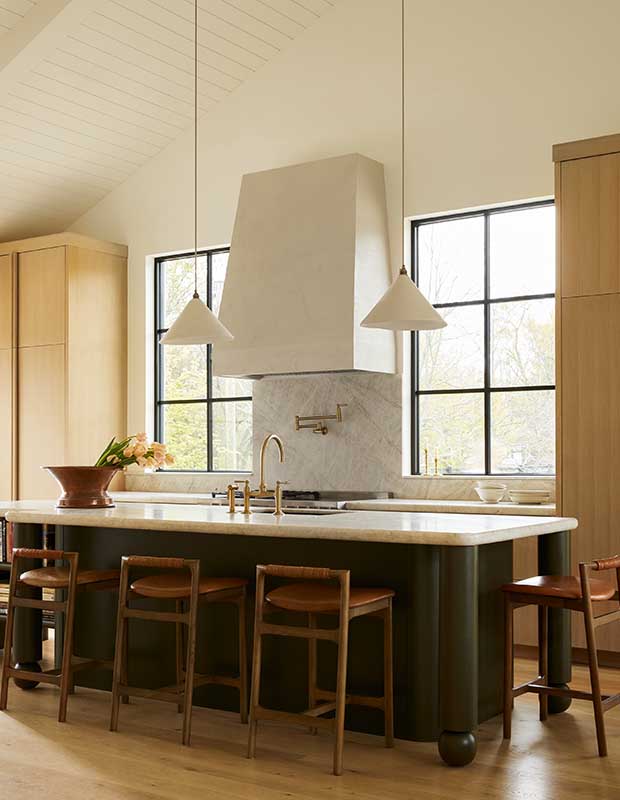 Photo of house featuring English design: A shot of a kitchen island. Behind it is a large white vent hood flanked by windows.
