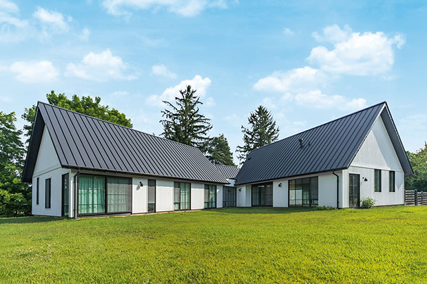 Photo of house featuring English design: Two wings of the house stick out at right angles to each other. They are white with black roofs, and they sit on a bright green lawn.